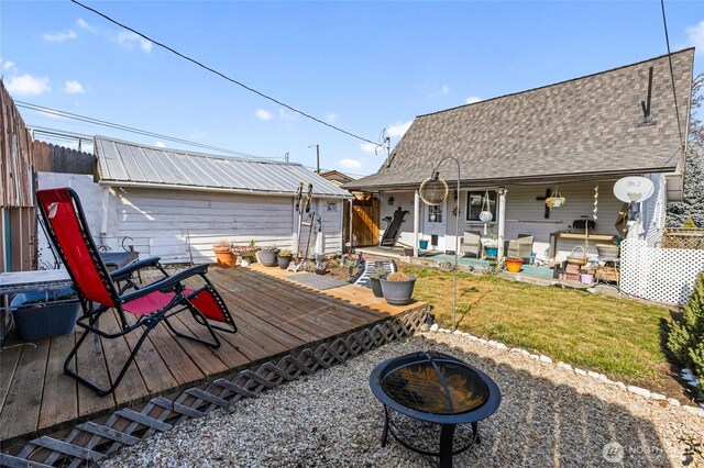 back of house featuring fence, an outdoor fire pit, a lawn, a deck, and an outdoor structure