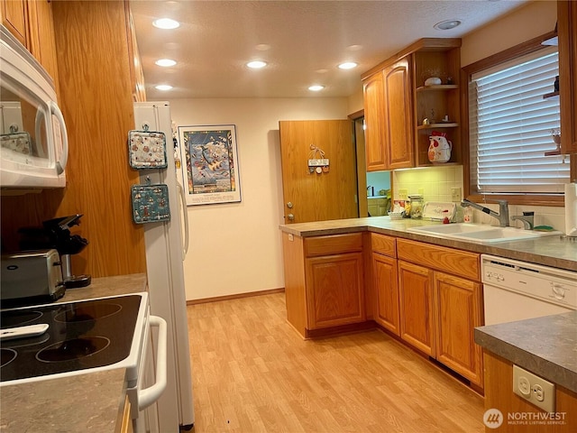 kitchen with a peninsula, white appliances, a sink, light wood-type flooring, and tasteful backsplash