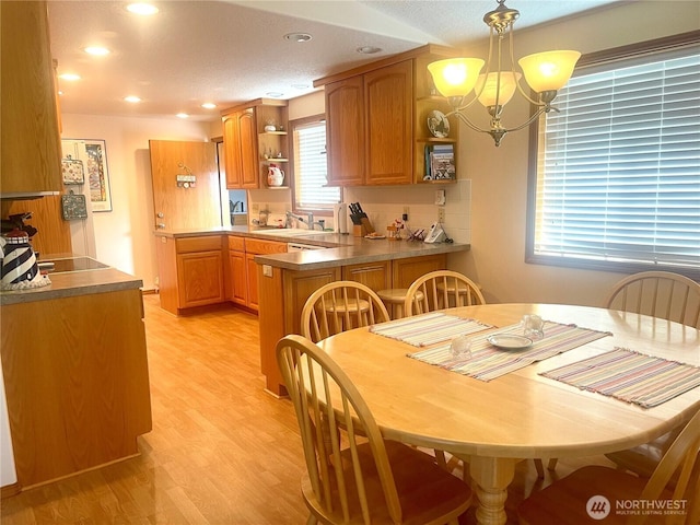 kitchen with light wood-style flooring, a peninsula, open shelves, brown cabinetry, and an inviting chandelier