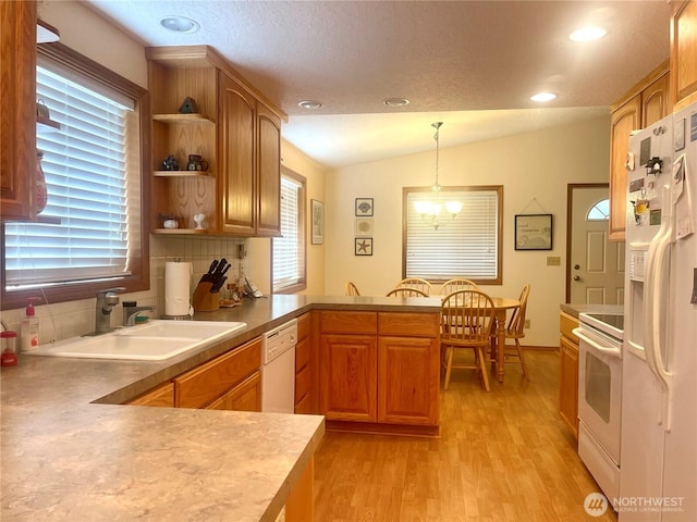 kitchen with white appliances, a peninsula, vaulted ceiling, light wood-type flooring, and a sink