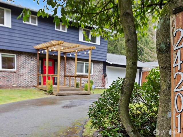 view of front of home with driveway, brick siding, an attached garage, and a pergola