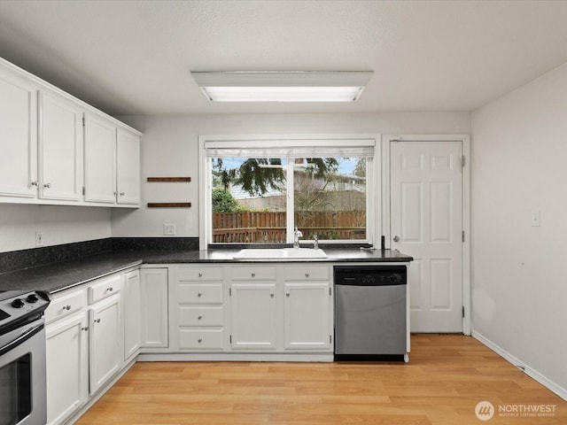 kitchen featuring stainless steel appliances, a sink, white cabinets, light wood-type flooring, and dark countertops