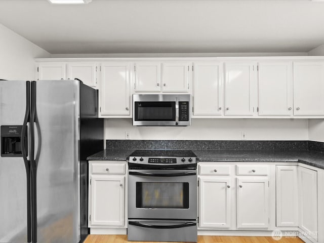 kitchen with white cabinets, light wood-style floors, stainless steel appliances, and dark stone countertops