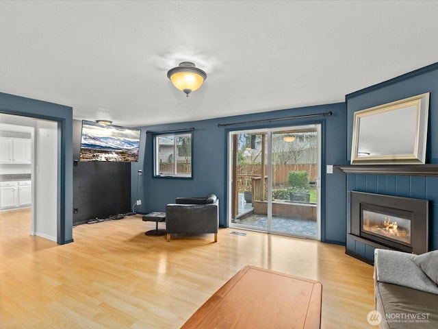 living area with baseboards, a tiled fireplace, visible vents, and light wood-style floors