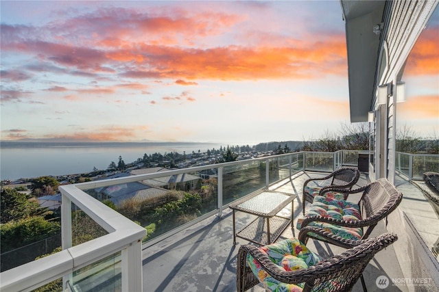 balcony at dusk featuring a water view