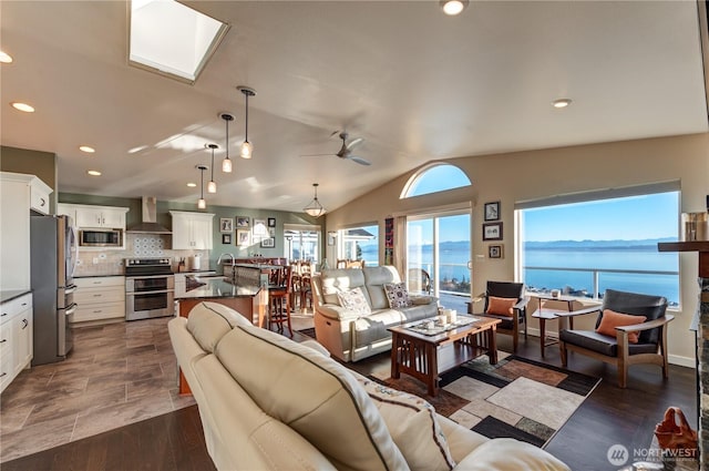 living area featuring dark wood finished floors, lofted ceiling with skylight, ceiling fan, a water view, and recessed lighting