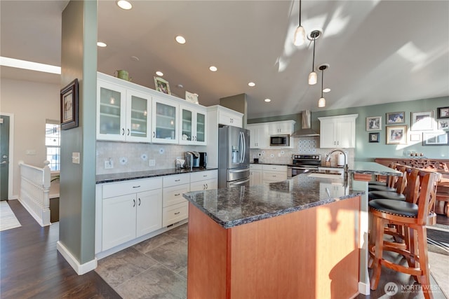 kitchen with stainless steel appliances, backsplash, a sink, and wall chimney range hood