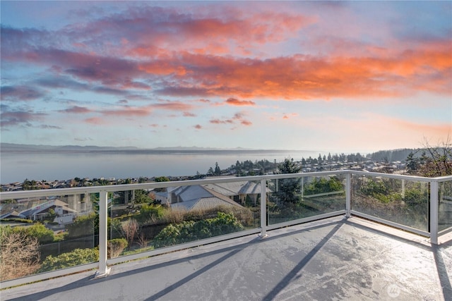 balcony at dusk featuring a water view