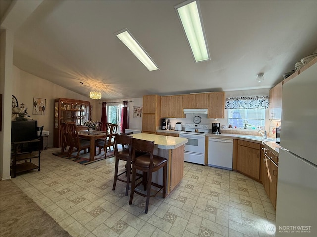 kitchen with white appliances, a kitchen island, light countertops, under cabinet range hood, and a sink