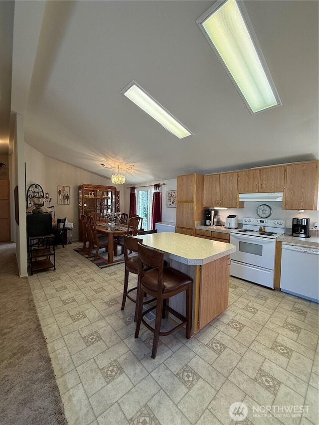 kitchen with light countertops, a kitchen island, white appliances, under cabinet range hood, and a kitchen bar