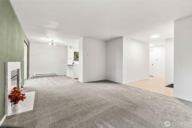 carpeted spare room with baseboards, a fireplace, a baseboard heating unit, and a sink