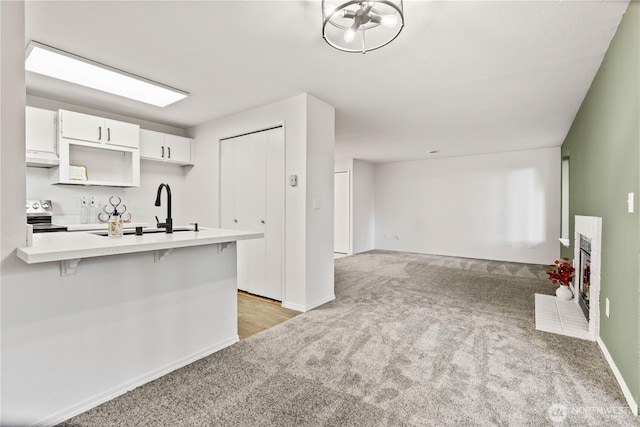 kitchen featuring light countertops, a fireplace with flush hearth, white cabinets, light carpet, and stainless steel electric range