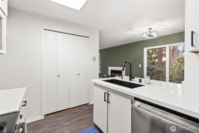 kitchen with dark wood-style flooring, a sink, light countertops, dishwasher, and a glass covered fireplace