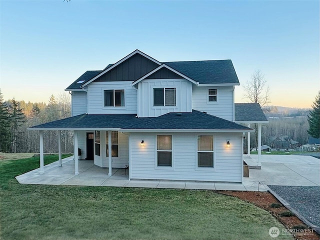 rear view of property featuring a patio, a shingled roof, board and batten siding, and a lawn