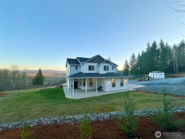 view of front of house featuring a patio, a detached garage, an outbuilding, a front lawn, and board and batten siding