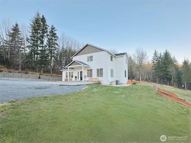 view of front of property featuring gravel driveway, central AC unit, board and batten siding, and a front yard