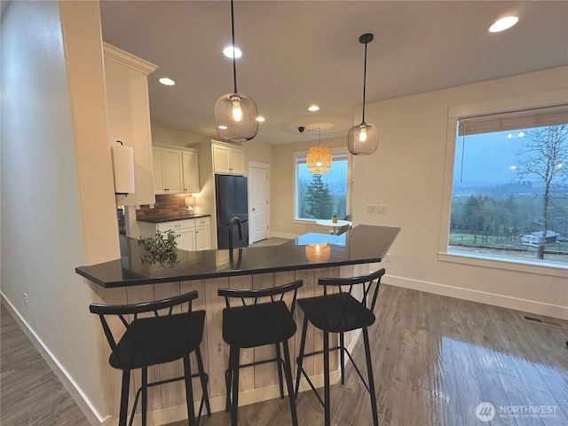 kitchen with a peninsula, black refrigerator, dark wood-style flooring, and dark countertops