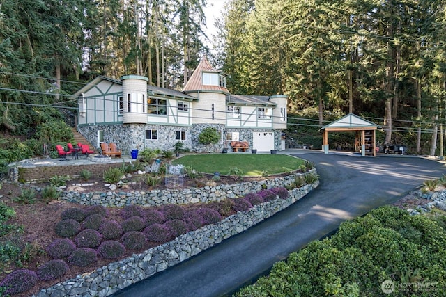 view of front of home featuring metal roof, stone siding, driveway, a front lawn, and a standing seam roof