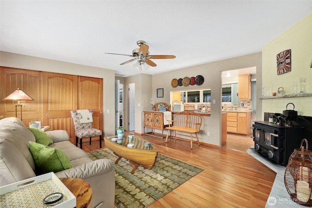 living area with light wood-style floors, a wood stove, baseboards, and a ceiling fan