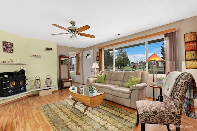 living area featuring visible vents, a fireplace, light wood-style flooring, and a ceiling fan