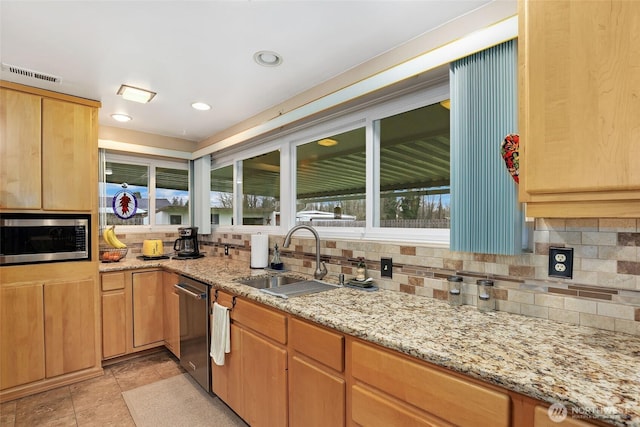 kitchen with tasteful backsplash, stainless steel microwave, a sink, and light stone counters