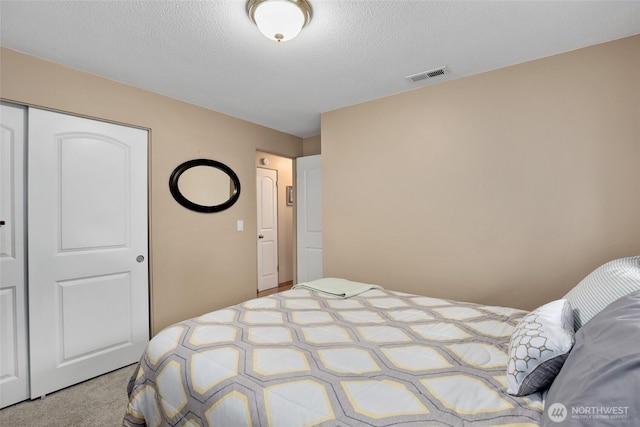 carpeted bedroom with a textured ceiling, a closet, and visible vents