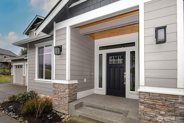 entrance to property featuring a garage, stone siding, and concrete driveway