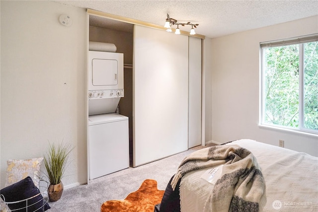 bedroom with stacked washer / drying machine, multiple windows, a textured ceiling, and carpet