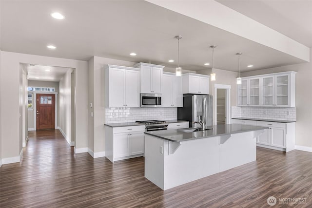 kitchen with dark wood finished floors, stainless steel appliances, glass insert cabinets, white cabinets, and an island with sink