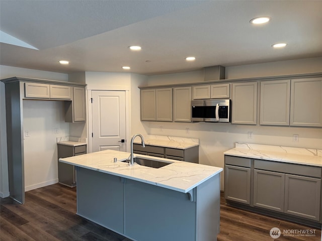 kitchen featuring stainless steel microwave, light stone countertops, gray cabinets, and a sink