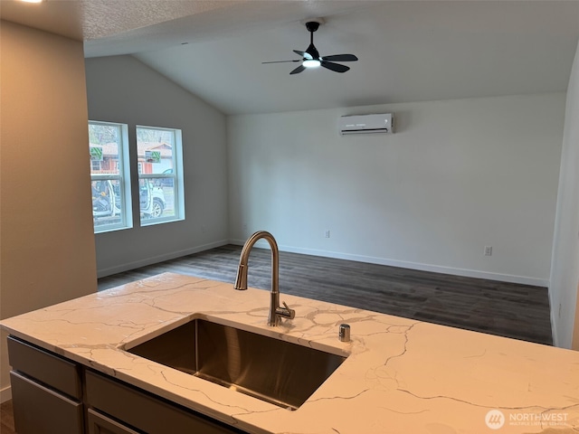 kitchen with light stone counters, open floor plan, a wall unit AC, and a sink