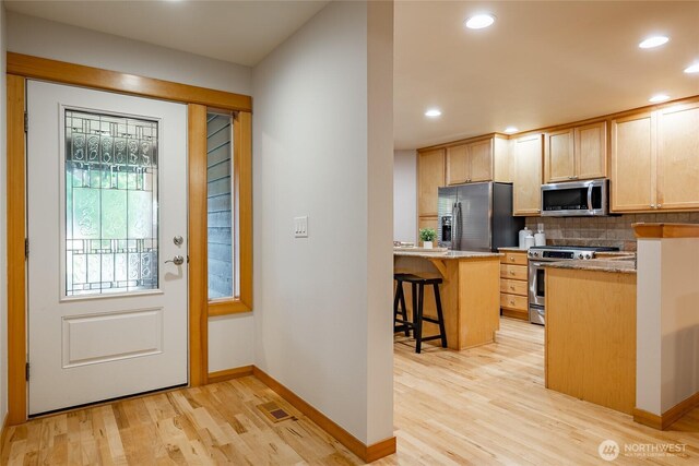 kitchen with tasteful backsplash, light brown cabinets, appliances with stainless steel finishes, and light wood-style flooring