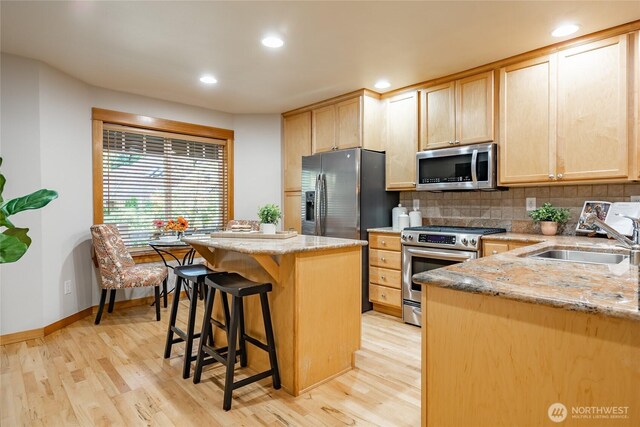 kitchen with light brown cabinets, stainless steel appliances, a sink, a center island, and tasteful backsplash