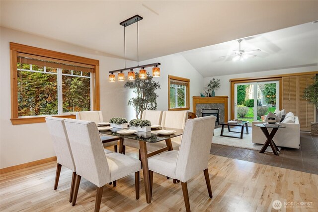 dining area featuring vaulted ceiling, baseboards, a fireplace, and light wood finished floors