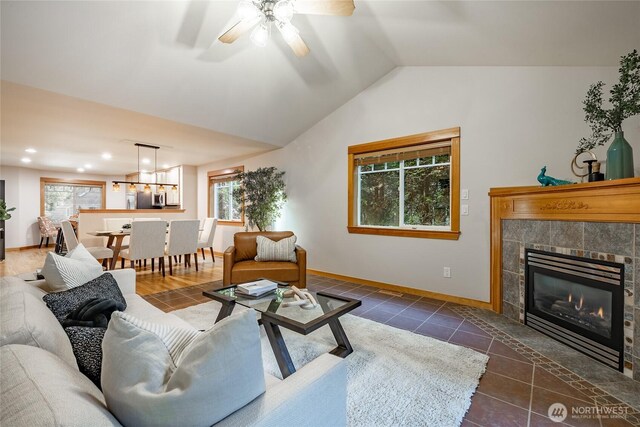 living area with dark tile patterned floors, a healthy amount of sunlight, vaulted ceiling, baseboards, and a tiled fireplace