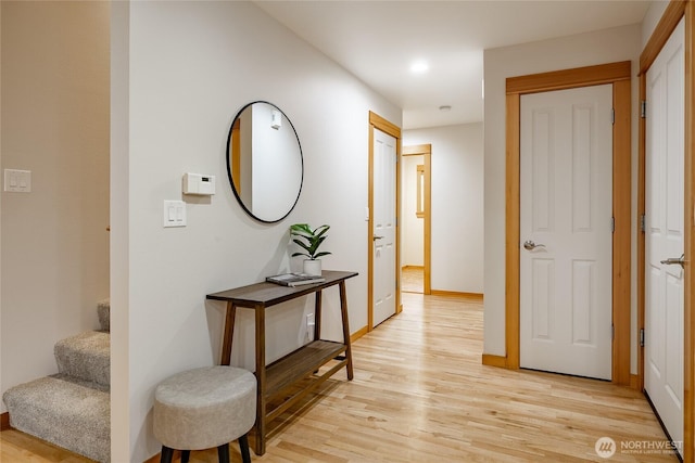 corridor with light wood-type flooring, stairs, and baseboards