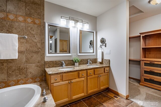 full bathroom with double vanity, tiled bath, a sink, and baseboards