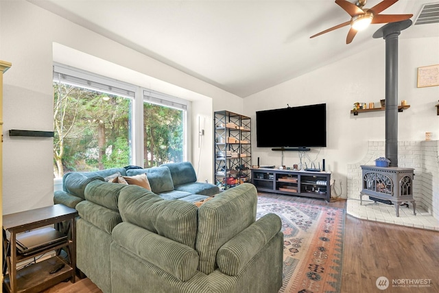 living room featuring a ceiling fan, wood finished floors, visible vents, lofted ceiling, and a wood stove