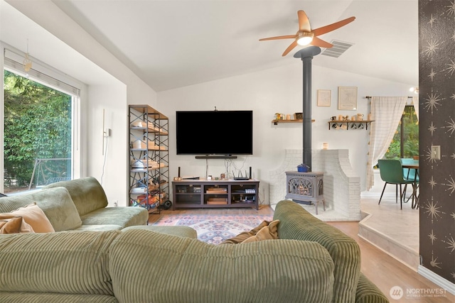 living room with visible vents, wood finished floors, a wood stove, and vaulted ceiling