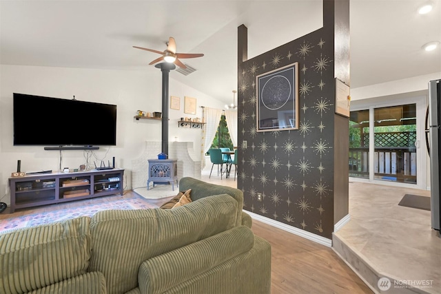 living room featuring wallpapered walls, baseboards, vaulted ceiling, a wood stove, and wood finished floors