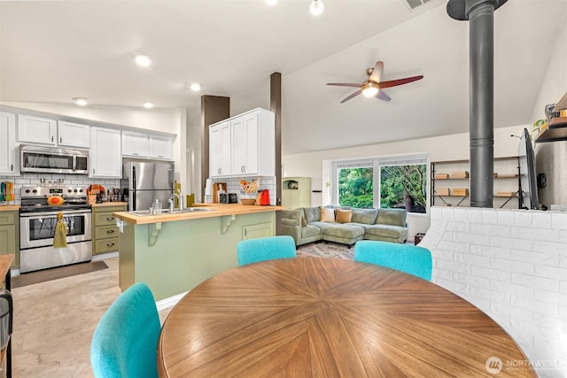 dining room featuring visible vents, ceiling fan, a wood stove, and vaulted ceiling