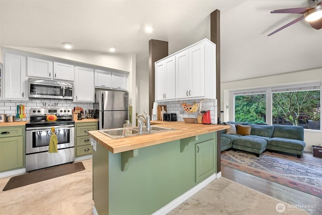 kitchen with wooden counters, green cabinets, vaulted ceiling, appliances with stainless steel finishes, and a sink