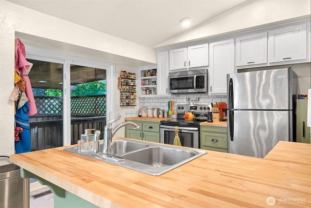 kitchen with lofted ceiling, a sink, stainless steel appliances, green cabinetry, and wooden counters