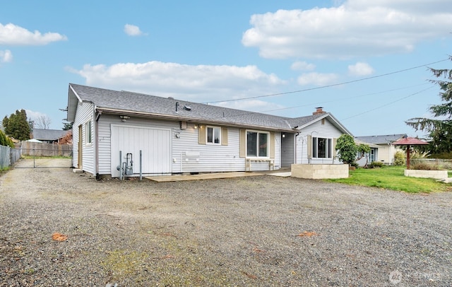 rear view of property with roof with shingles, gravel driveway, a chimney, and fence