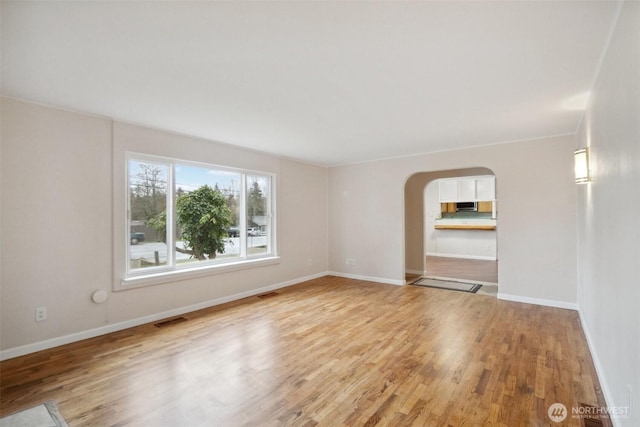 unfurnished room with arched walkways, visible vents, light wood-type flooring, and baseboards