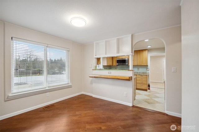 kitchen with arched walkways, stainless steel microwave, visible vents, and wood finished floors