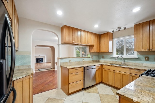 kitchen featuring dishwasher, black fridge, light tile patterned floors, and a sink