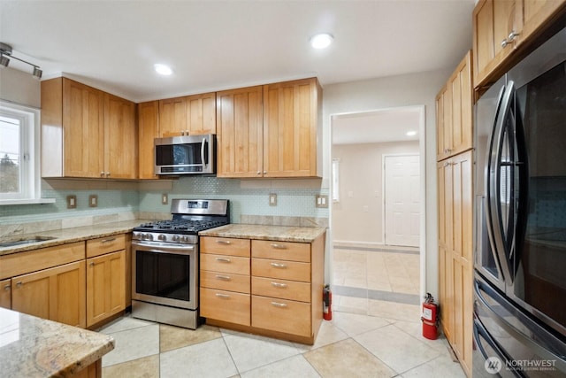 kitchen with light stone counters, light tile patterned flooring, tasteful backsplash, and stainless steel appliances