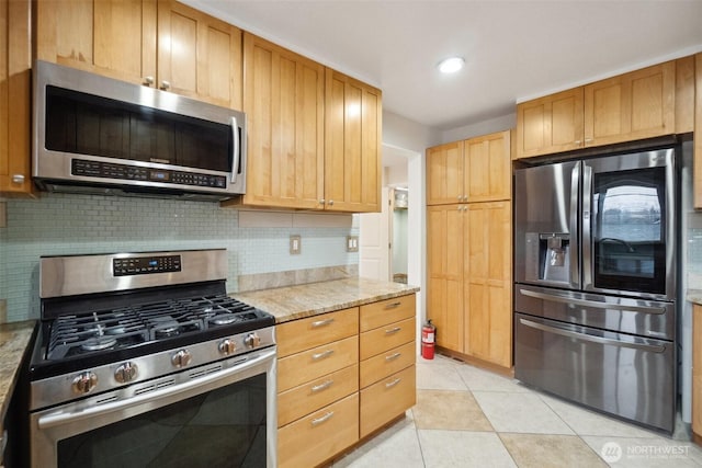 kitchen featuring light tile patterned flooring, decorative backsplash, appliances with stainless steel finishes, and light stone countertops