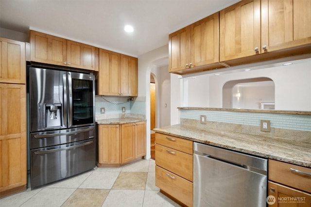 kitchen with light stone counters, light tile patterned floors, arched walkways, stainless steel appliances, and backsplash